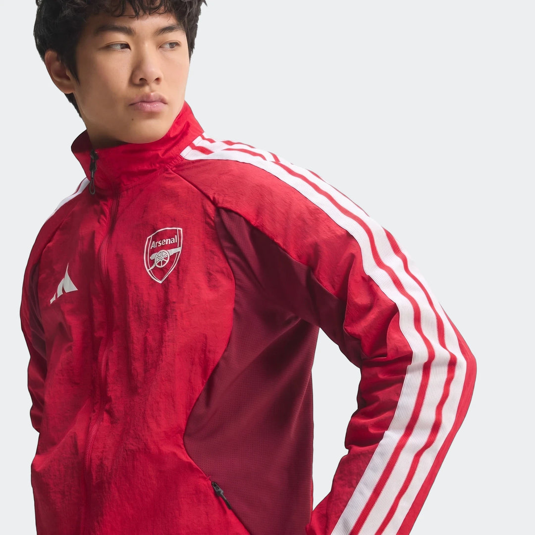 Young man wearing a red Arsenal Fc Home Anthem Jacket with white stripes and the club crest.