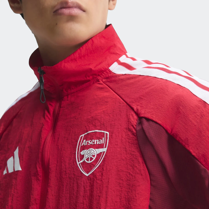 Close-up of a model wearing a red Arsenal FC Home Anthem Jacket with white shoulder stripes and club logo.
