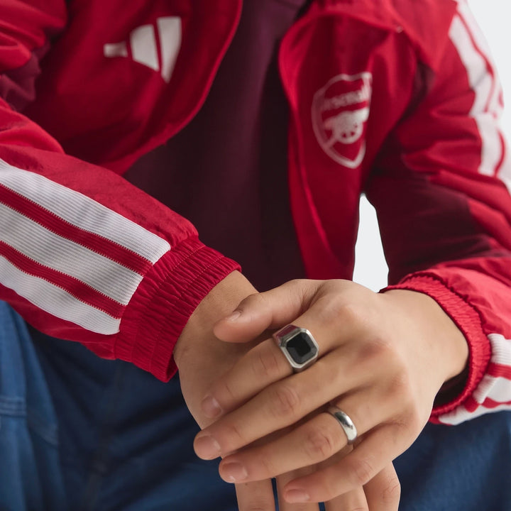 Close-up of a person wearing a red Adidas Arsenal FC Home Anthem Jacket with white stripes and club crest, featuring hands
