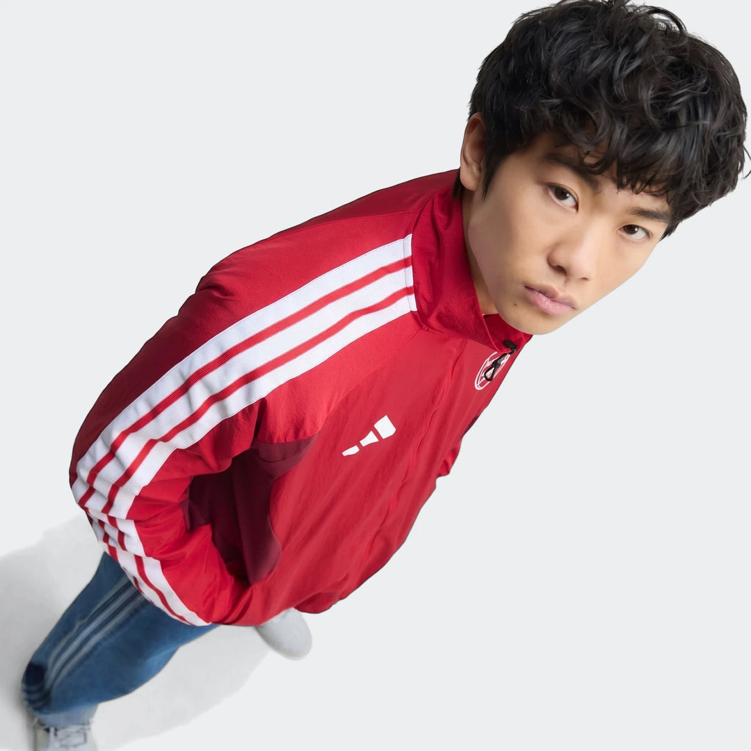 Overhead view of a young man wearing the red Adidas Arsenal Fc Home Anthem Jacket with white stripes and blue jeans.