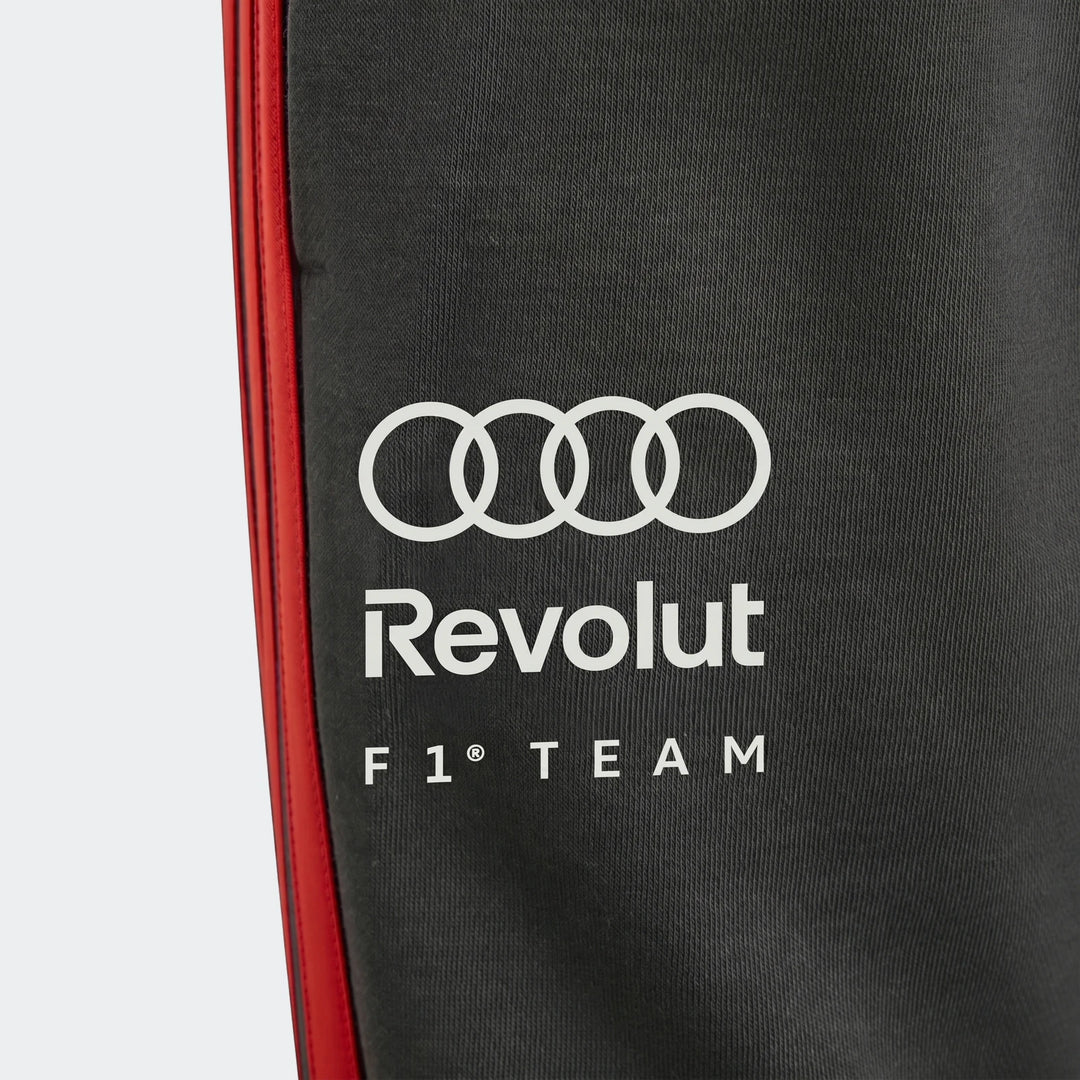 Close-up of Audi Revolut F1 Team Dna Pants Youth, dark grey with a red side stripe and white Audi and Revolut F1 Team logos.