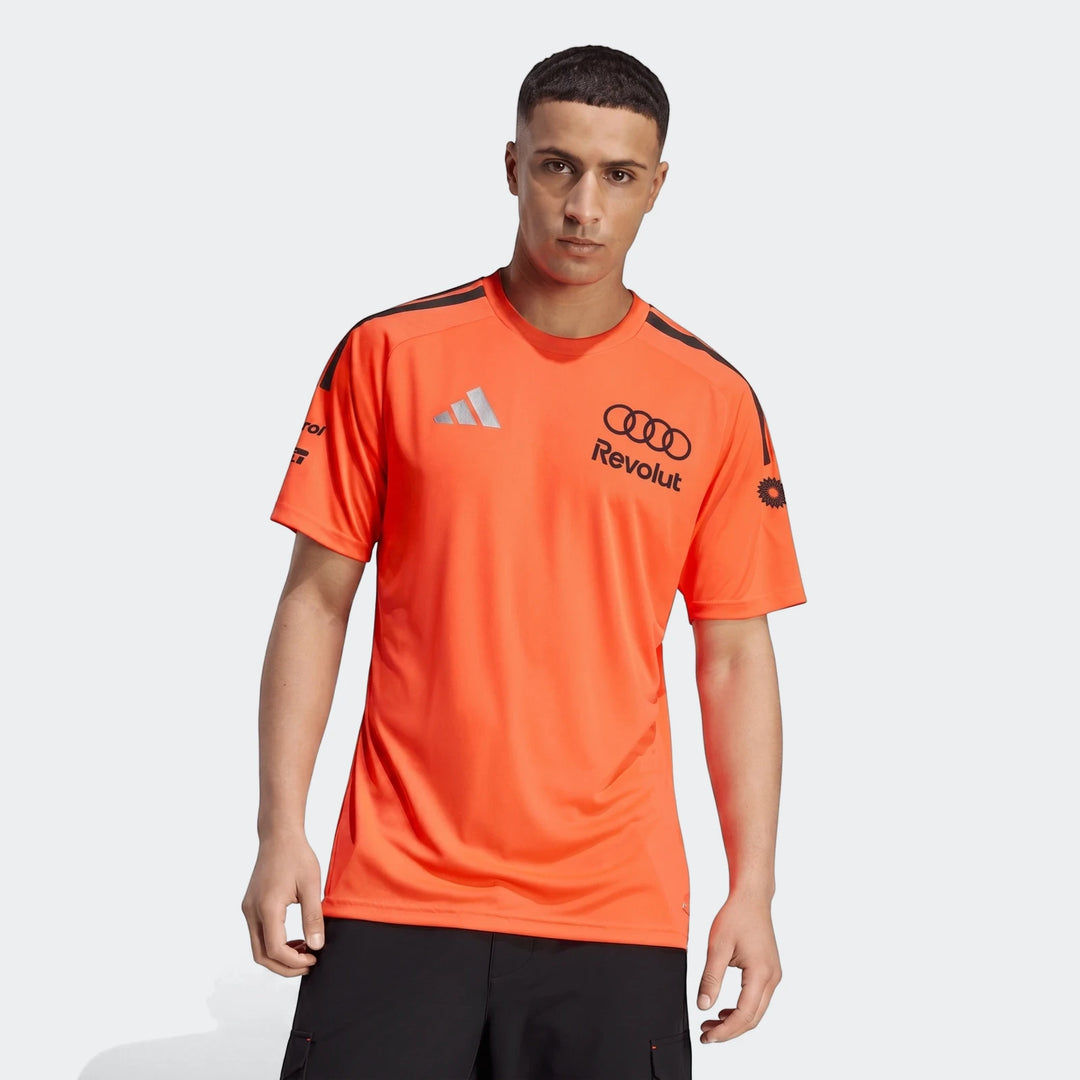 Male model wearing an orange Audi Revolut F1 Team Setup T-Shirt with black logos and shoulder stripes.
