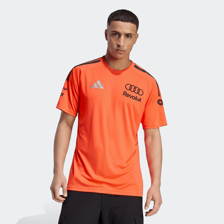Male model wearing an orange Audi Revolut F1 Team Setup T-Shirt with black logos and shoulder stripes.