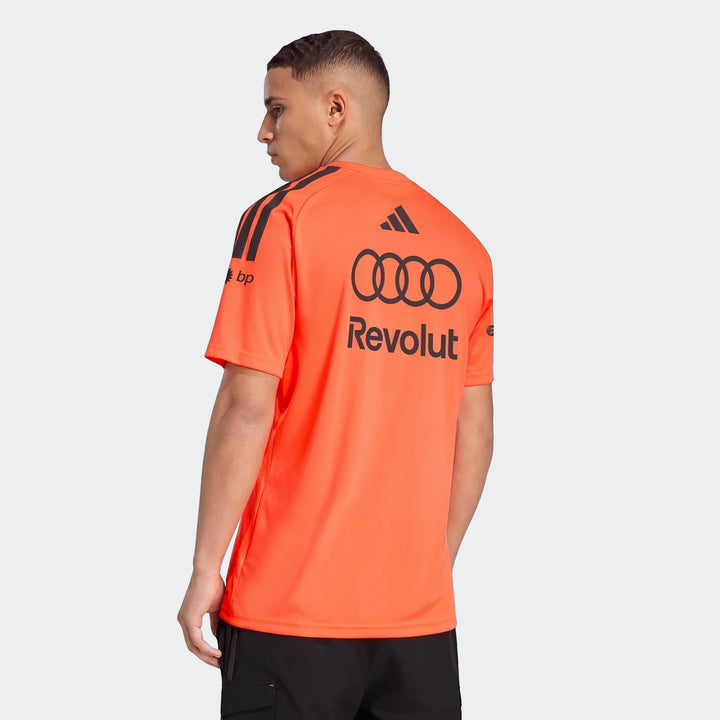 Male model wearing an orange Audi Revolut F1 Team Setup T-Shirt, showcasing black Adidas, Audi, and Revolut branding on the