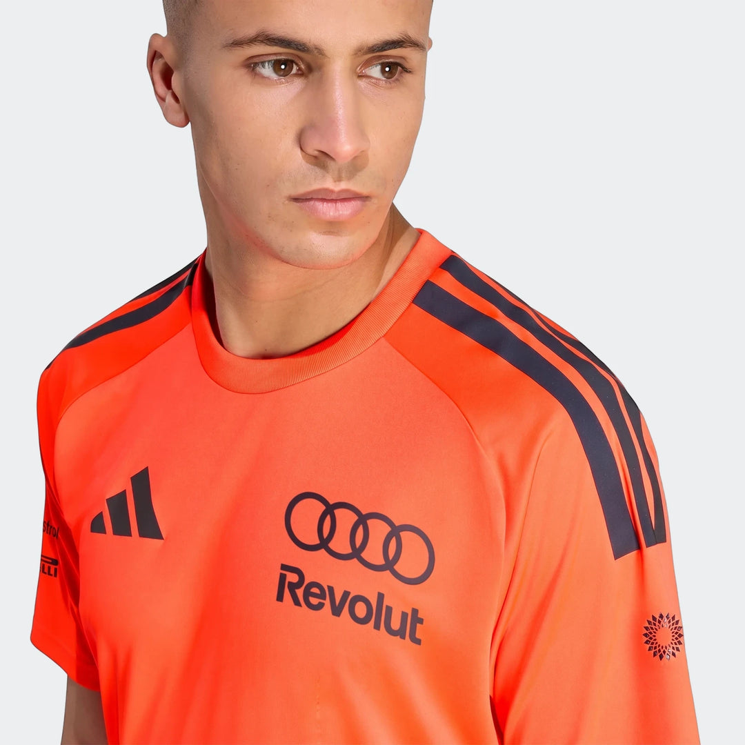 Male model in an orange Audi Revolut F1 Team Setup T-Shirt featuring black Adidas, Audi, and Revolut logos.
