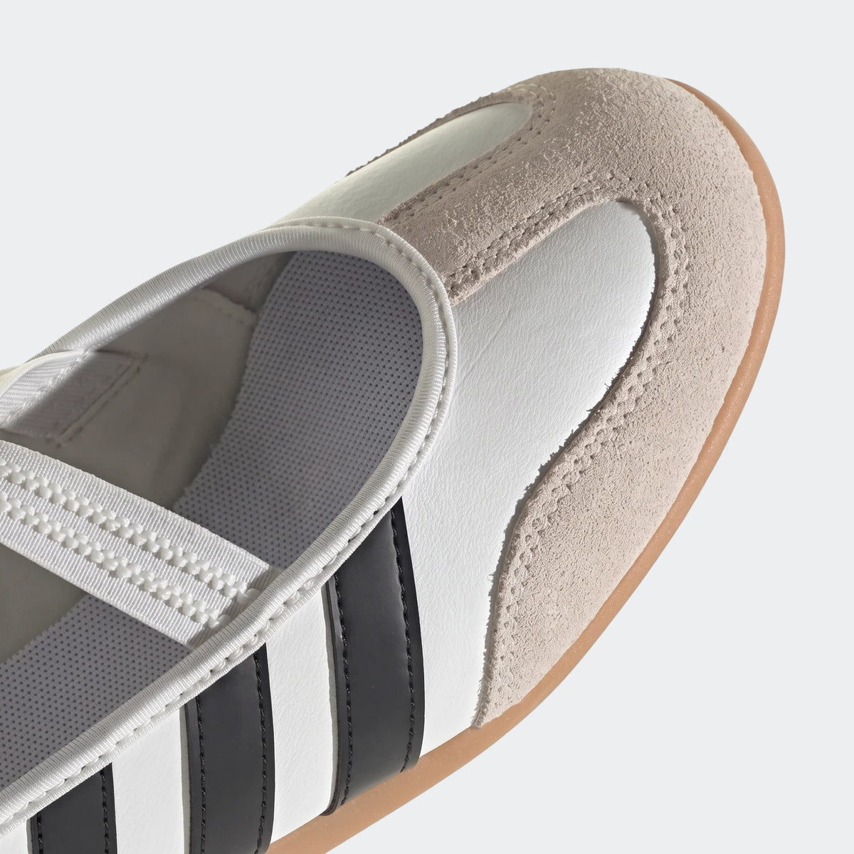 Close-up of a white, black, and beige suede Adidas Barreda Mary Jane shoe with iconic black three stripes.