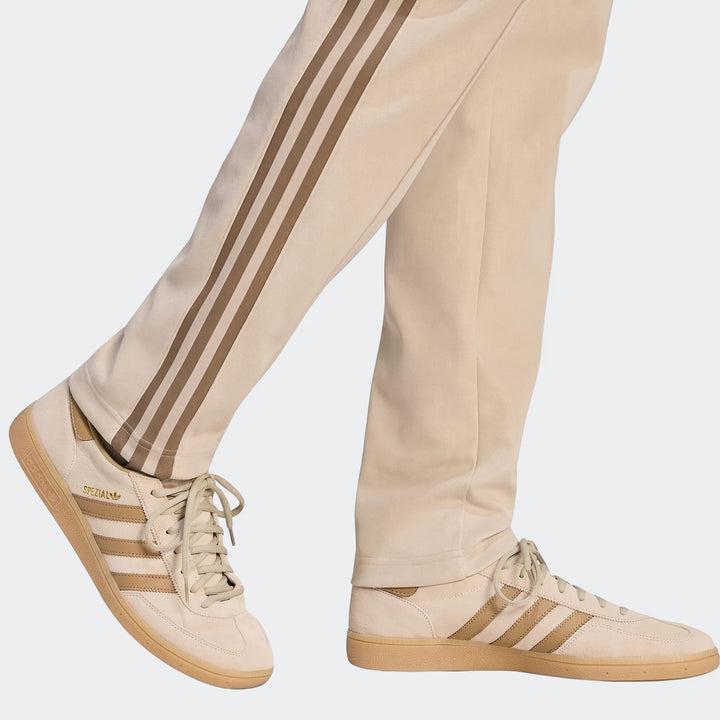 Beige Classic Track Pants with brown stripes, paired with beige Adidas Spezial sneakers, shown from a mid-leg view.