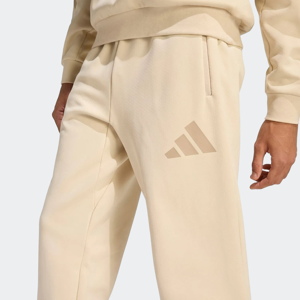 Close-up of beige men's Adidas Z.N.E. track pants, featuring the three-bar logo and side zippered pockets.