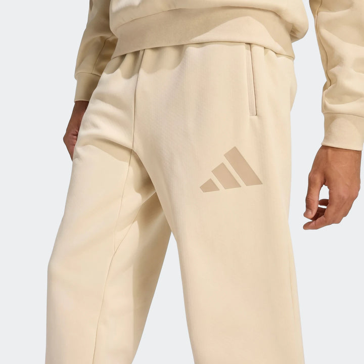 Close-up of beige men's Adidas Z.N.E. track pants, featuring the three-bar logo and side zippered pockets.