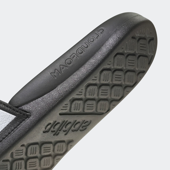 Close-up of a black Adidas Adilette slide sandal sole, featuring embossed brand logos and a distinctive textured pattern.
