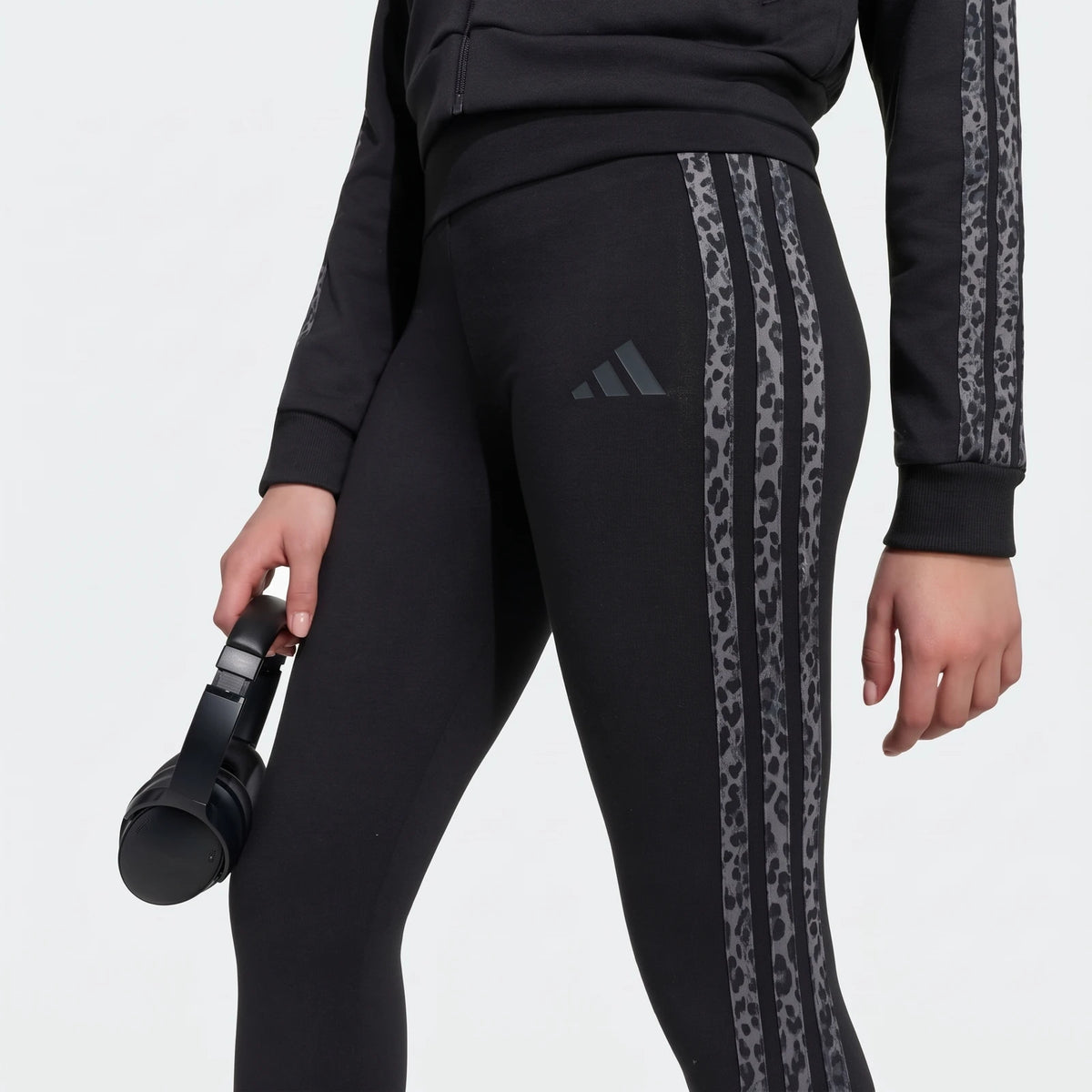 Close-up of black Adidas Animal Leggings with leopard print stripes, worn by a person also in a matching black jacket,