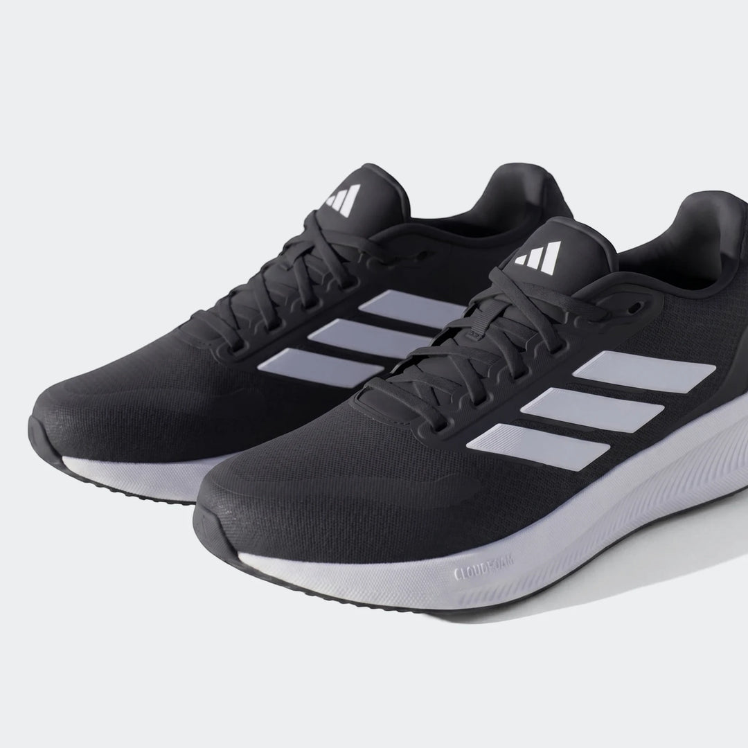 Pair of black Adidas sneakers with white three stripes and white Cloudfoam soles, shown at an angle on a concrete surface.