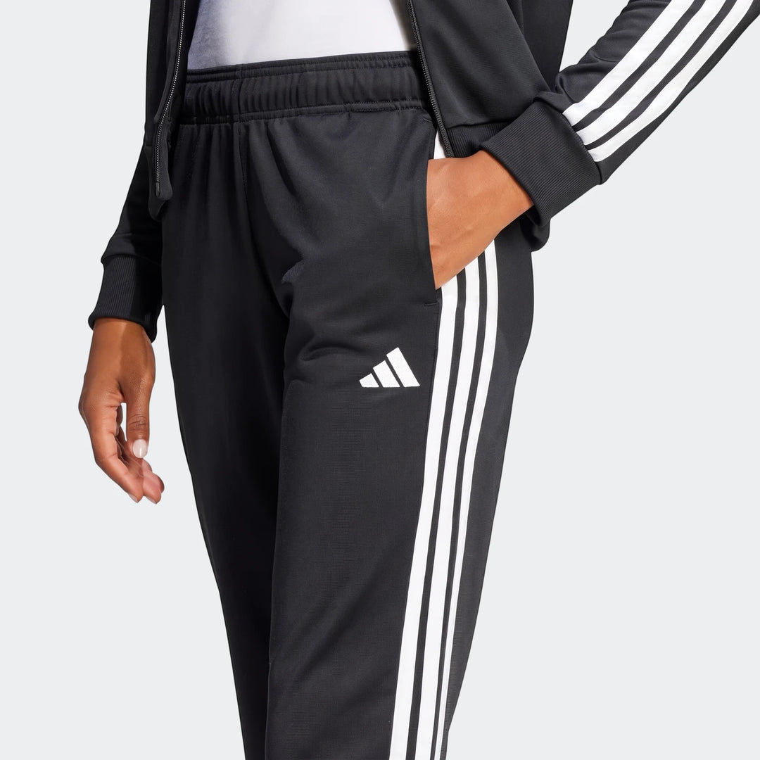 Close-up of a person wearing black Adidas Dayready tracksuit pants and jacket, featuring white three stripes and an Adidas