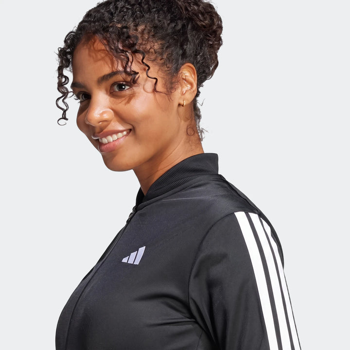 Close-up of a smiling woman wearing a black Adidas Dayready Tracksuit jacket with white stripes on the arm.