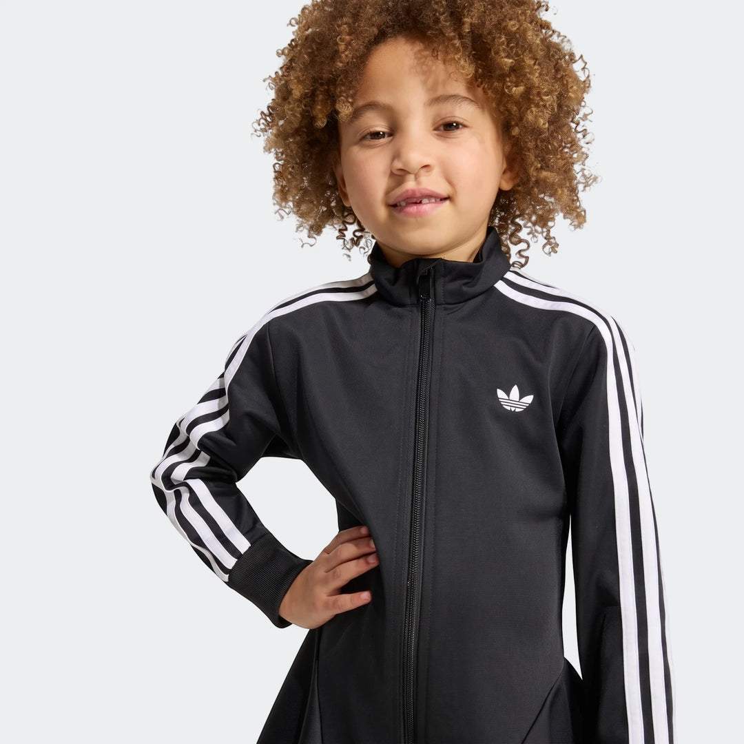 Young girl in black Adidas Firebird Longsleeve Dress, featuring white three stripes on the sleeves and a white trefoil logo.