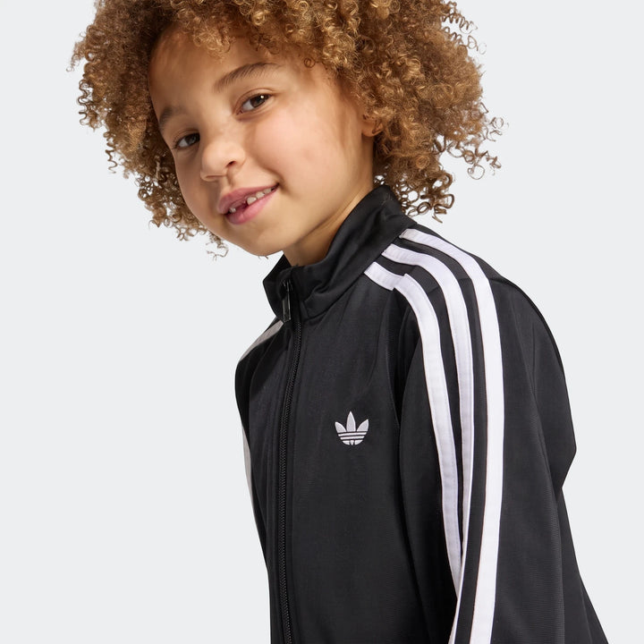 Young child wearing a black Adidas Firebird Longsleeve Dress with white stripes and Trefoil logo.