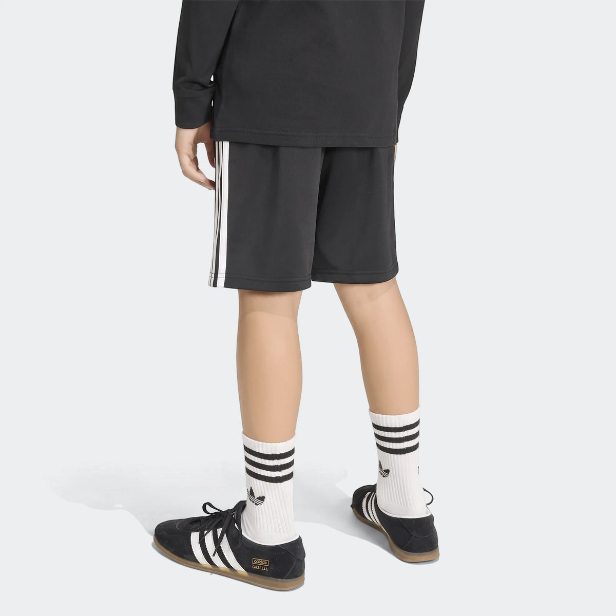 Back view of black Adidas Firebird shorts with white stripes worn by a person, paired with white striped socks and black
