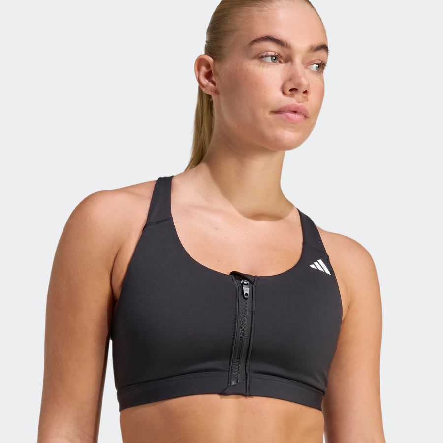 A woman models a black Adidas Optime Essentials Workout Zip-Front Medium Support Bra, featuring a front zipper and white