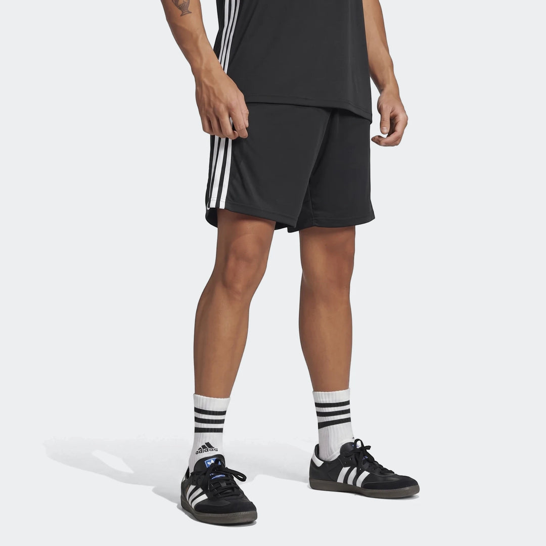Black Adidas shorts with white stripes, white athletic socks, and black Adidas Samba sneakers on a model.