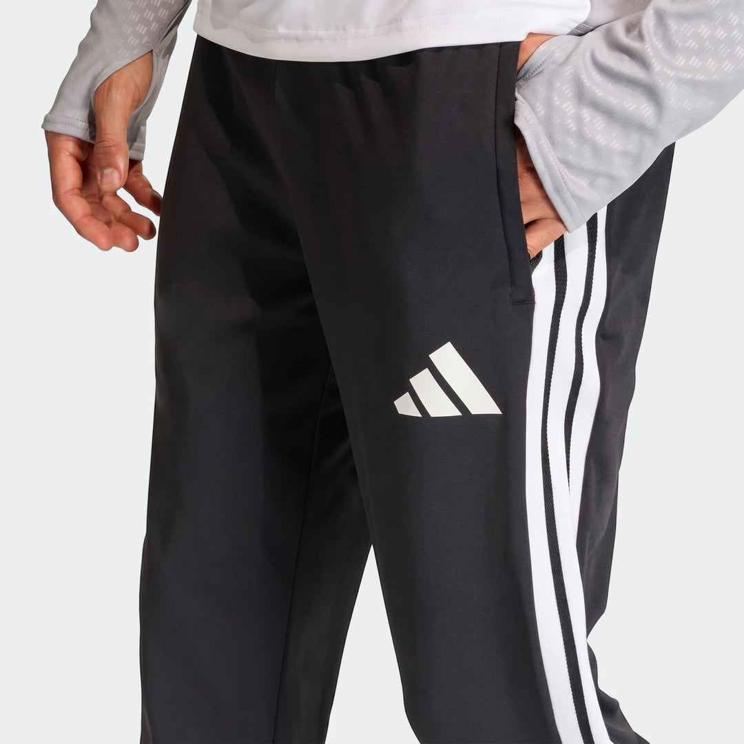 Close-up of black Adidas Tiro 26 Competition Training Pants with white stripes and logo, worn by a person with hand in