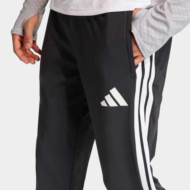 Close-up of black Adidas Tiro 26 Competition Training Pants with white stripes and logo, worn by a person with hand in