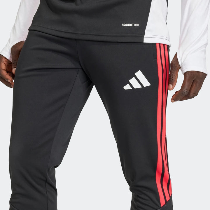 Close-up of a person wearing black Adidas Tiro 26 Competition Training Pants with red three stripes down the side.
