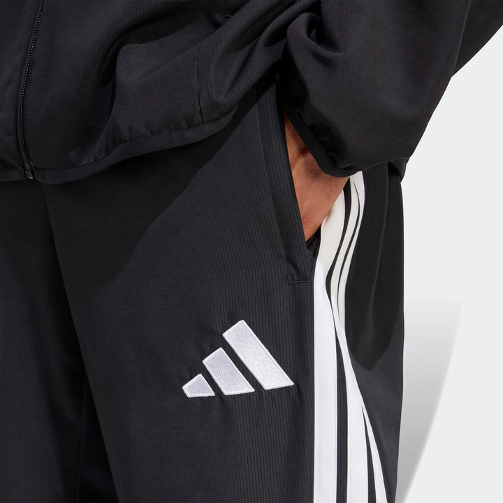Black Adidas Tiro 26 League Presentation Pants, featuring the white logo and three stripes, worn by a person with a hand in