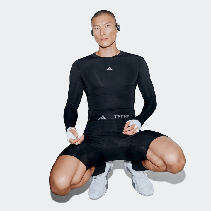 Male model wearing a black Adidas Z.N.E. Track Top and matching compression shorts, crouching in a gym with hand wraps.