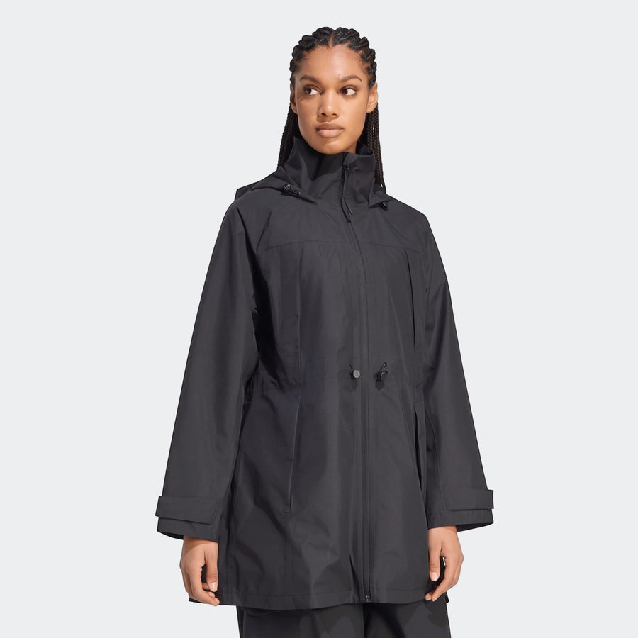 Woman wearing a black City Rain Parka, a hooded lightweight jacket, standing with a neutral expression. The parka features a