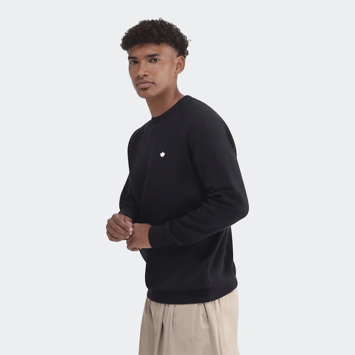 Black Essentials Crew Sweatshirt for men, featuring a white logo, worn by a model and paired with beige trousers.
