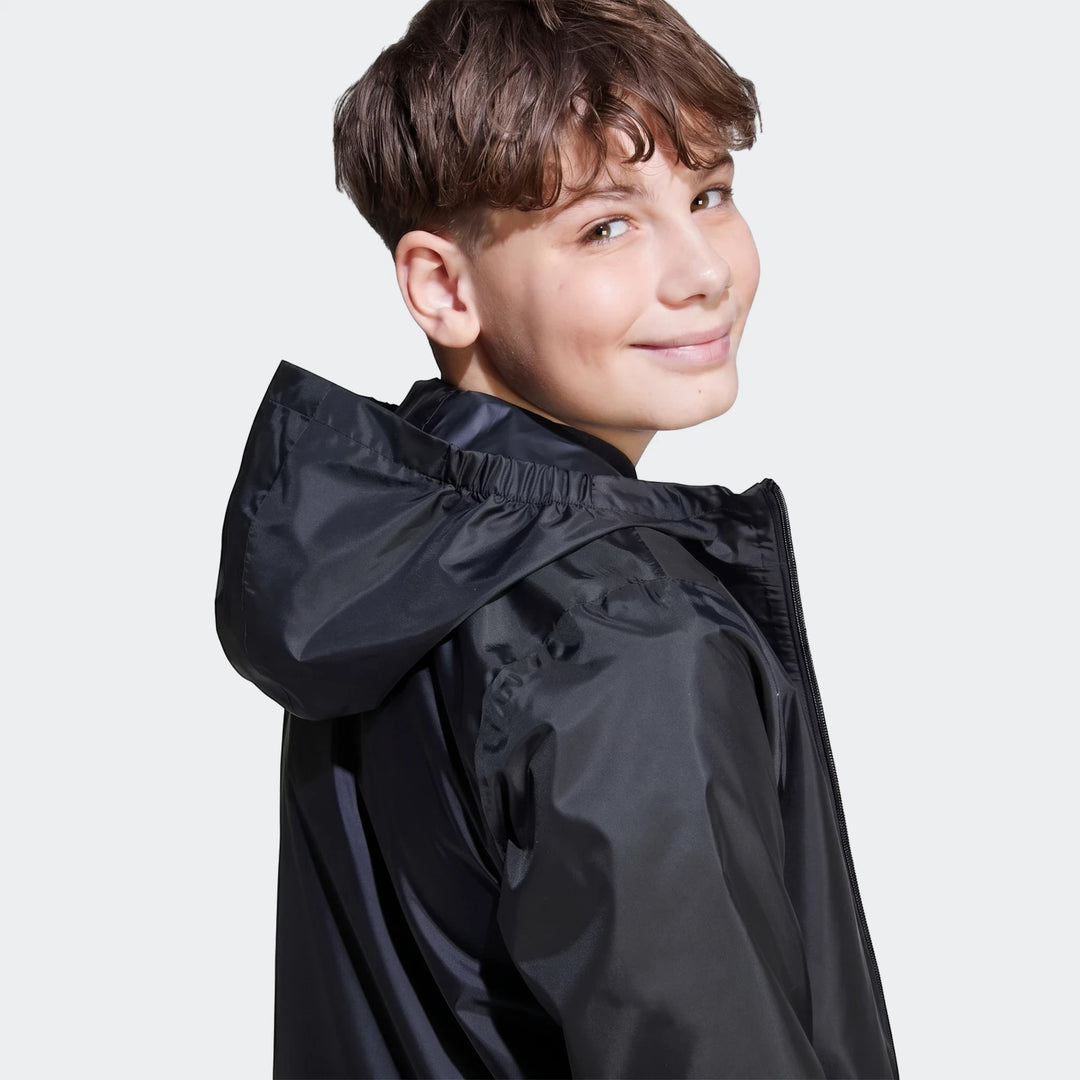Young boy wearing a black kids' rain jacket, looking over his shoulder against a plain background. The jacket features a