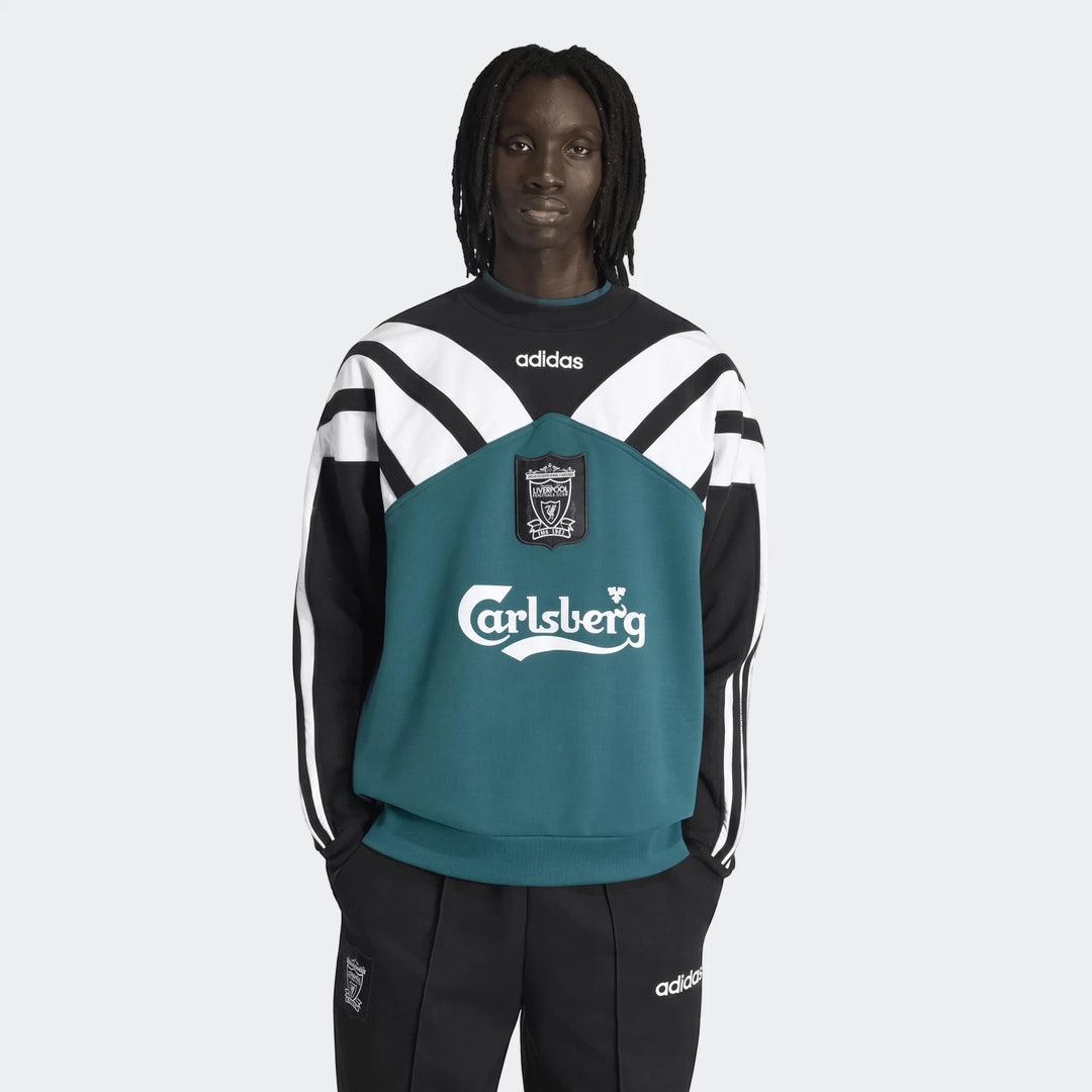 Black male model wearing a black, white, and teal Adidas Liverpool FC 1995 sweatshirt with track pants, front view.