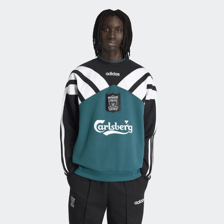 Black male model wearing a black, white, and teal Adidas Liverpool FC 1995 sweatshirt with track pants, front view.