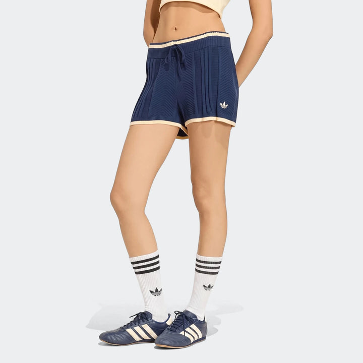 Blue Adidas cable knit shorts with white and yellow trim, drawstring, and Adidas logo, worn by a model standing.