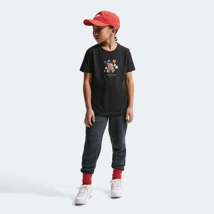 Boy wearing a black Nike K Nsw Boxy t-shirt with a colorful sports graphic, dark pants, a red cap, and white sneakers.