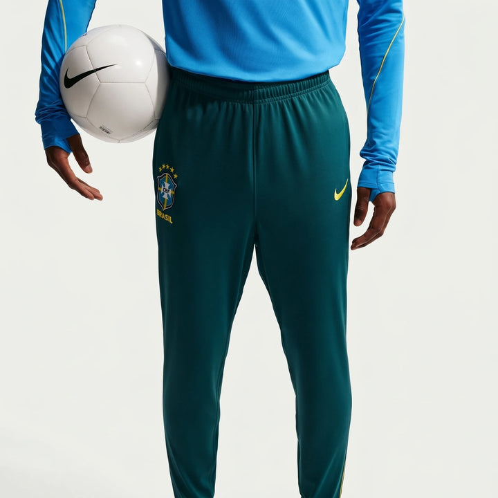 Closeup of a person wearing Brazil Academy Pro Green Men's Nike Dri-Fit Soccer Track Pants, holding a white soccer ball.