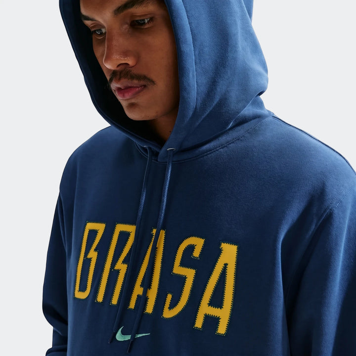 Close-up of a man wearing a Brazil Club blue men's Nike soccer French Terry pullover hoodie with yellow 'BRASIL' text.