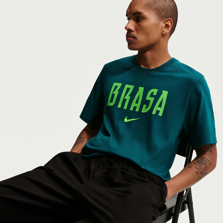 Men's dark teal green Nike soccer t-shirt featuring a vibrant lime green 'BRASA' logo and swoosh, worn by a model seated.
