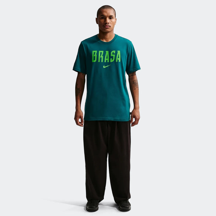 Full body shot of a man wearing a Brazil Green Men's Nike Soccer T-Shirt. The teal t-shirt features green 'BRASA' lettering
