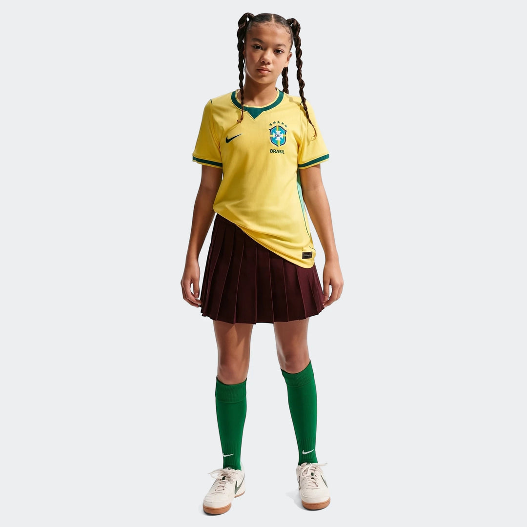 Young person in yellow Brazil National Team 2026 Stadium Home Nike Dri-Fit soccer jersey, brown skirt, green socks, and