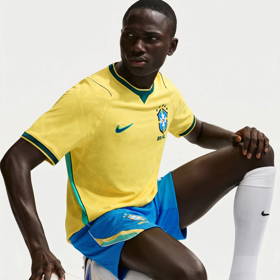 Dark-skinned model wearing a yellow Brazil National Team 2026 Match Home Men's Nike Aero-Fit soccer jersey, blue shorts, and