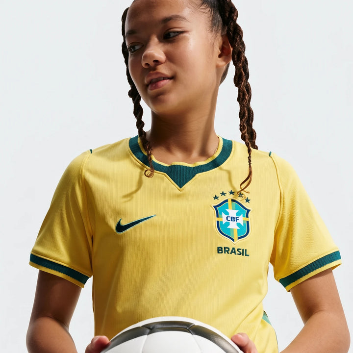 Young girl wearing a yellow Brazil National Team 2026 Stadium Home Nike Dri-Fit soccer jersey, holding a soccer ball.