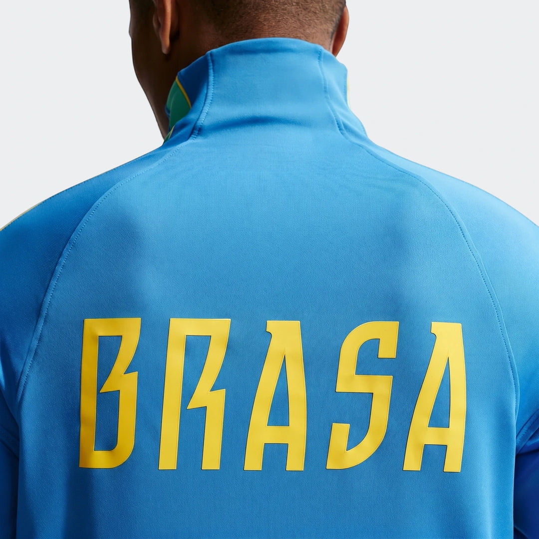 Rear view of a men's Brazil Strike Blue Nike Dri-Fit Soccer Drill Top, featuring a yellow 'BRASA' logo on the back.