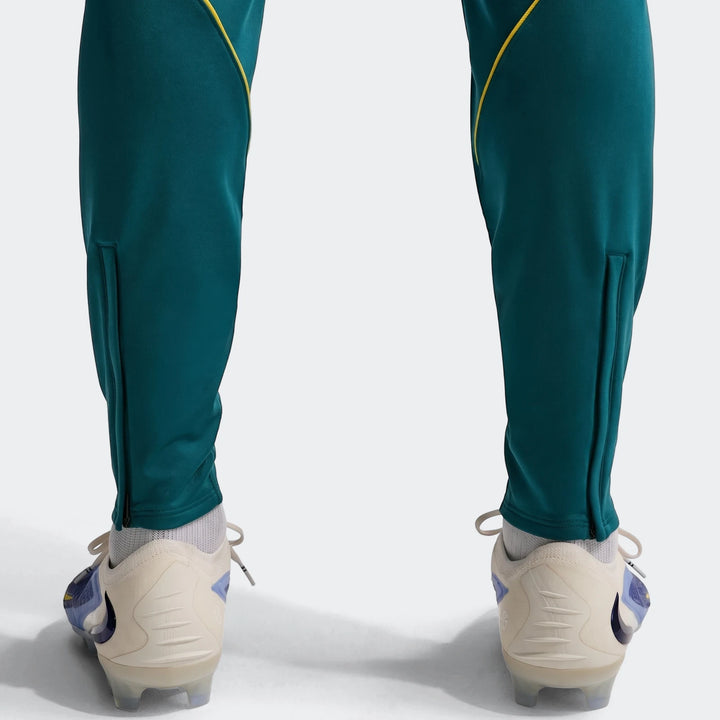 Close-up of men's Brazil Strike green Nike Dri-Fit soccer knit pants with yellow stripes and light-colored soccer cleats.