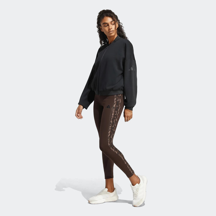 Female model in brown All-Over Print Infill Leggings with leopard print side stripes, styled with a black bomber jacket and