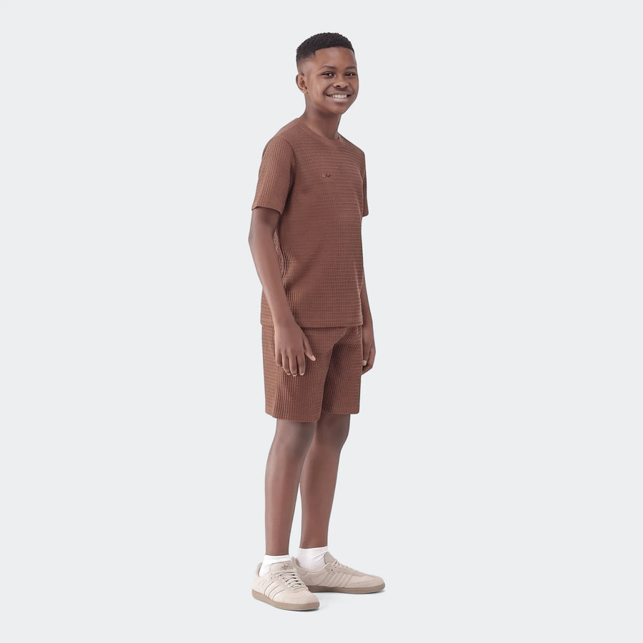 Young boy models a brown waffle knit short-sleeve t-shirt and matching shorts set, smiling casually on a white background.