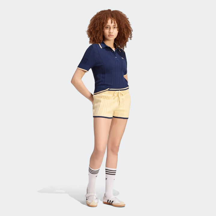 A model wears a navy blue Cable Knit Cali Tee Polo and yellow knit shorts, styled with white socks and strap shoes. Full
