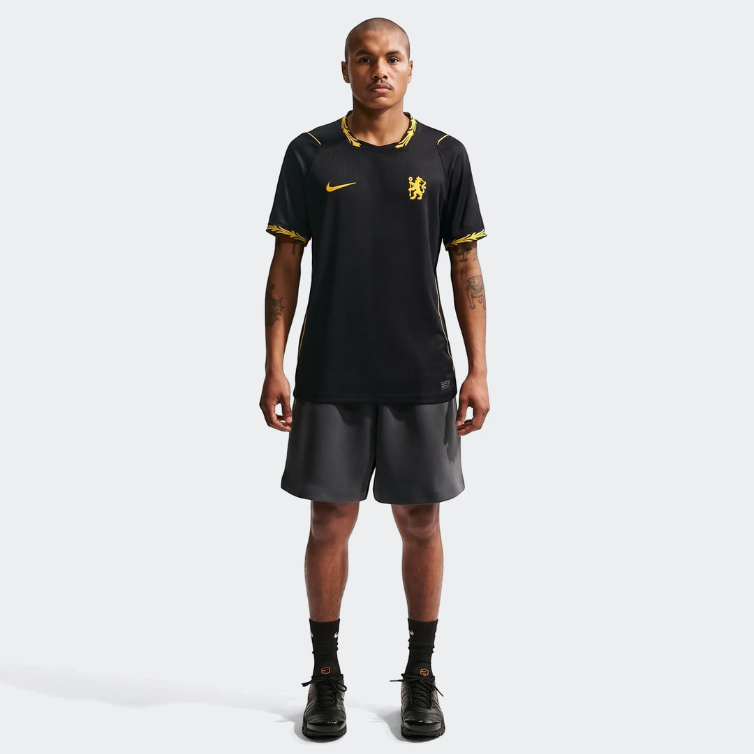 A male model wears the black and yellow Chelsea FC 2026/27 Stadium Away Men's Nike Dri-Fit Soccer Replica Jersey, shorts,