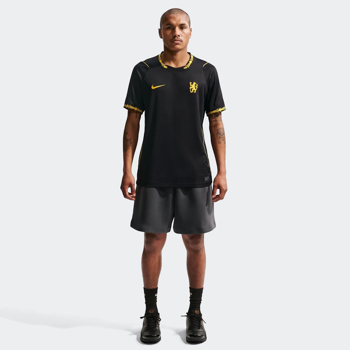 A male model wears the black and yellow Chelsea FC 2026/27 Stadium Away Men's Nike Dri-Fit Soccer Replica Jersey, shorts,