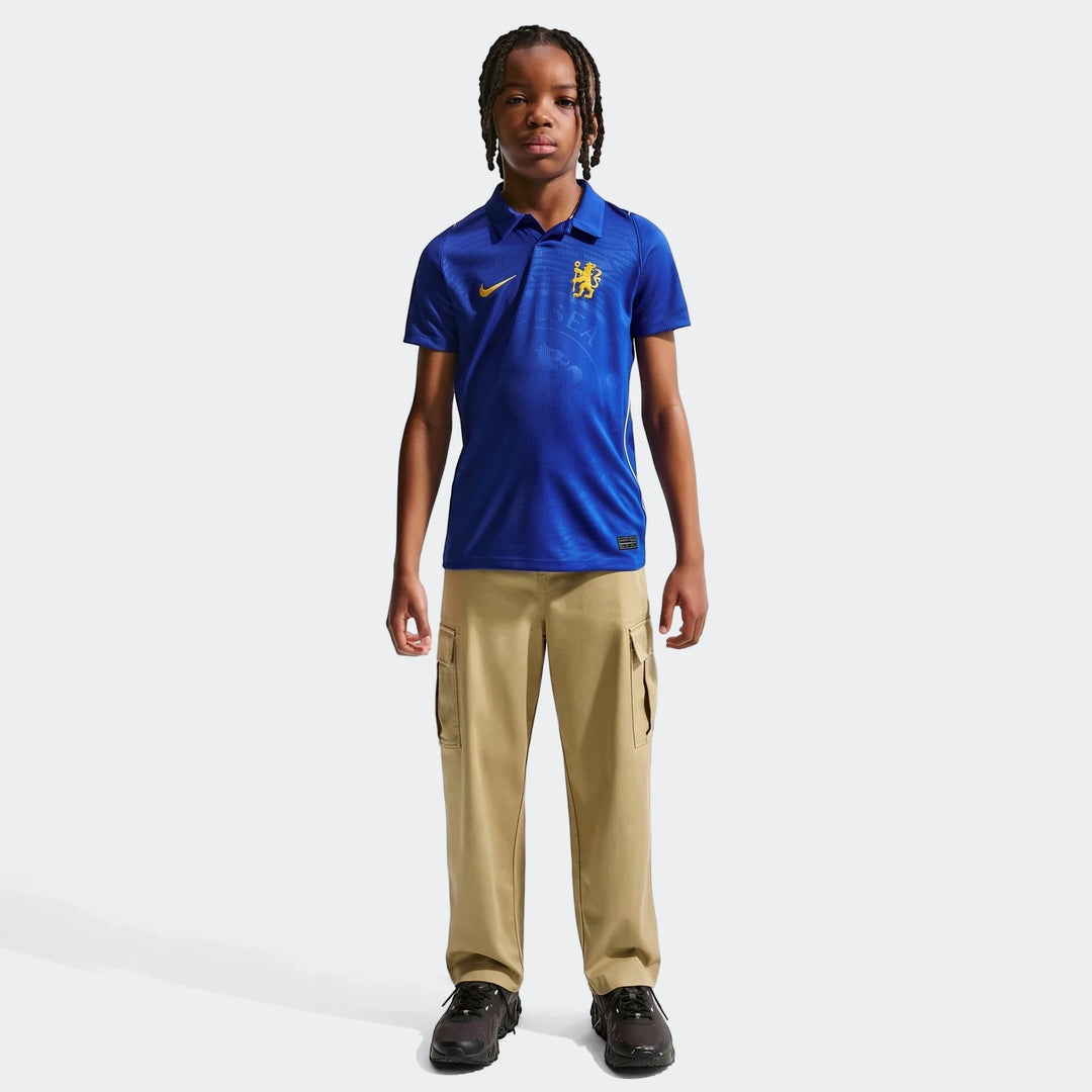 Young boy wearing a blue Nike Chelsea FC 2026/27 Stadium Home soccer replica jersey with khaki cargo pants.